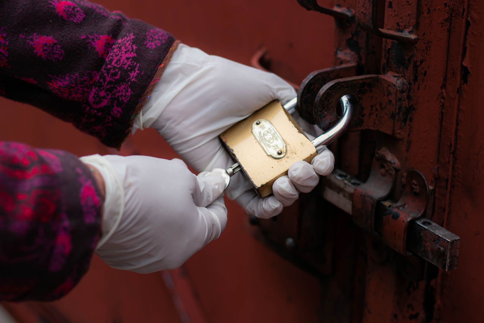 Mains gantées qui tournent une clé dans un cadenas rouillé