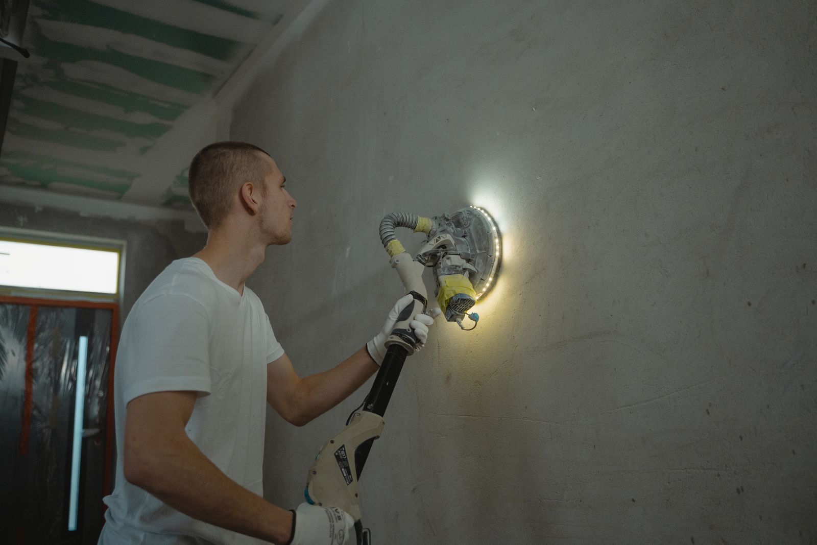Mains tenant une ponceuse girafe pour poncer un mur de placo