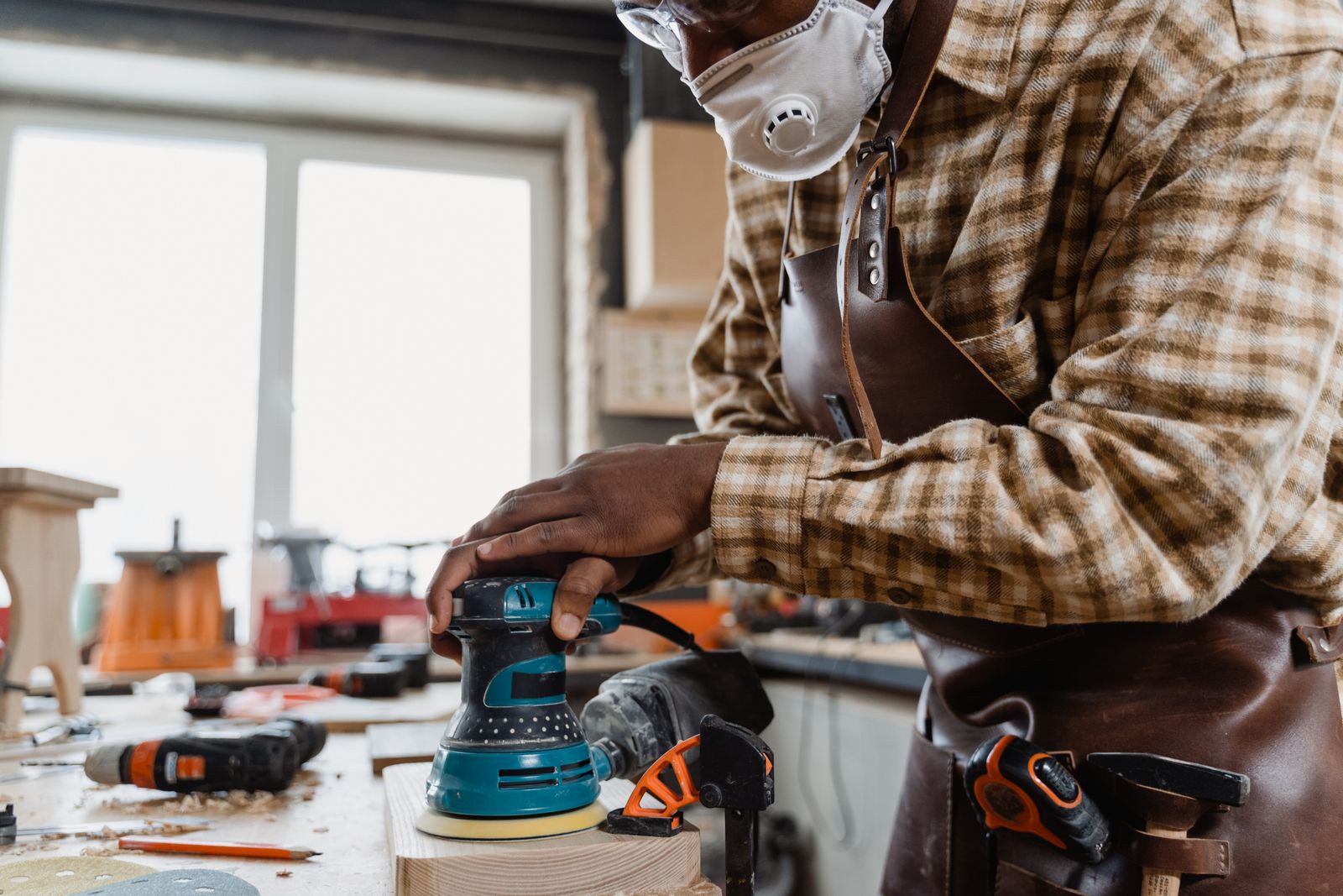 Mains guidant une ponceuse excentrique sur une planche en bois
